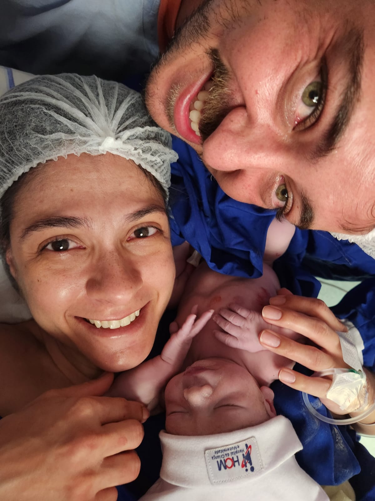 Família com a mãe segurando a filha recém-nascida, em um momento de emoção e cuidado.